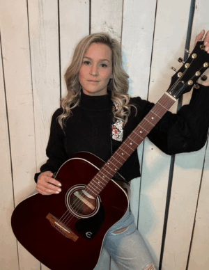 BB Anne with maroon guitar standing in front of a whitewash board background